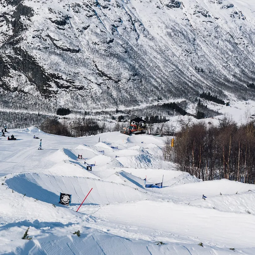 Preparert snowboardløype med hopp og porter ligger i et snødekt fjellområde.